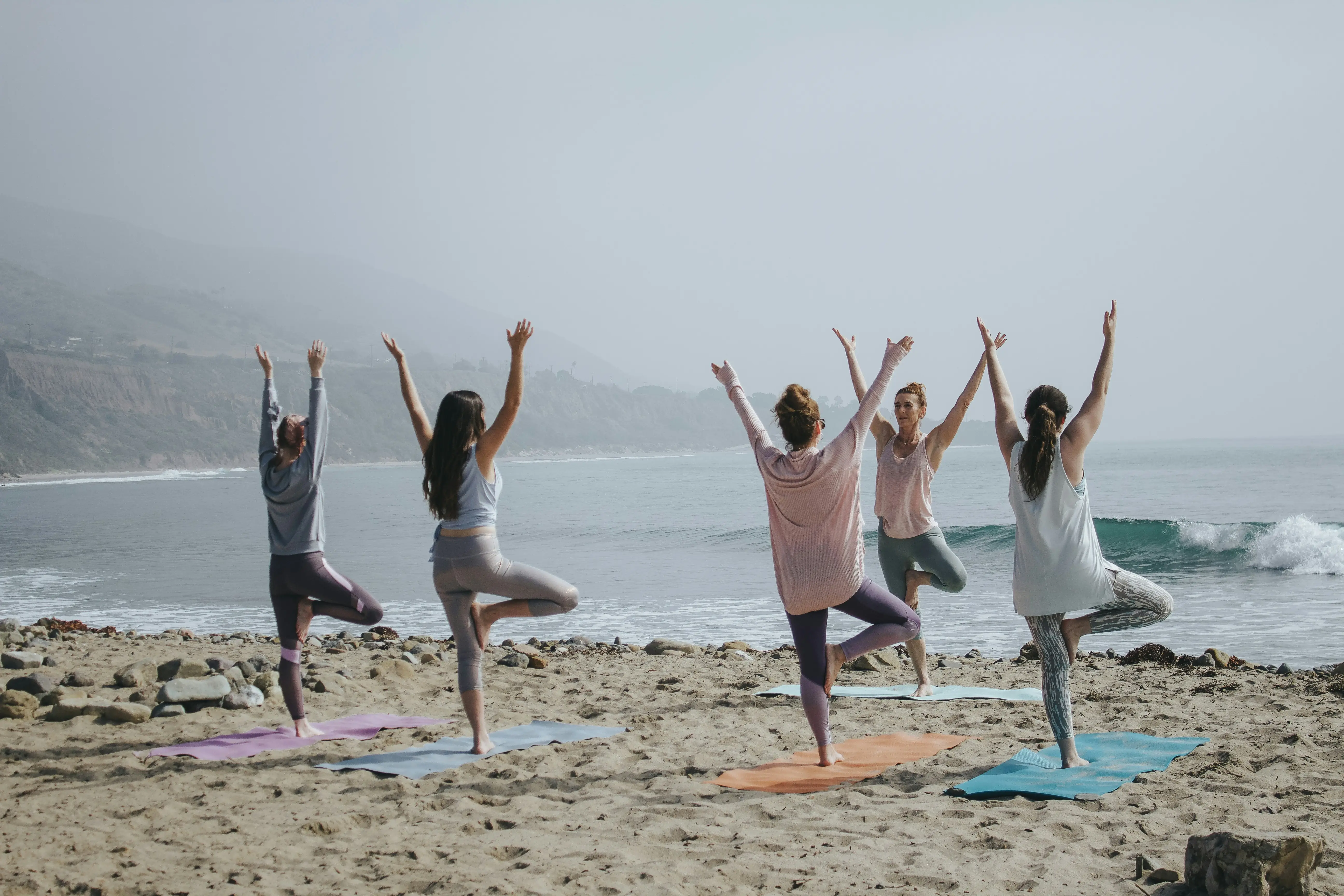 A group of five people doing yoga on the beach