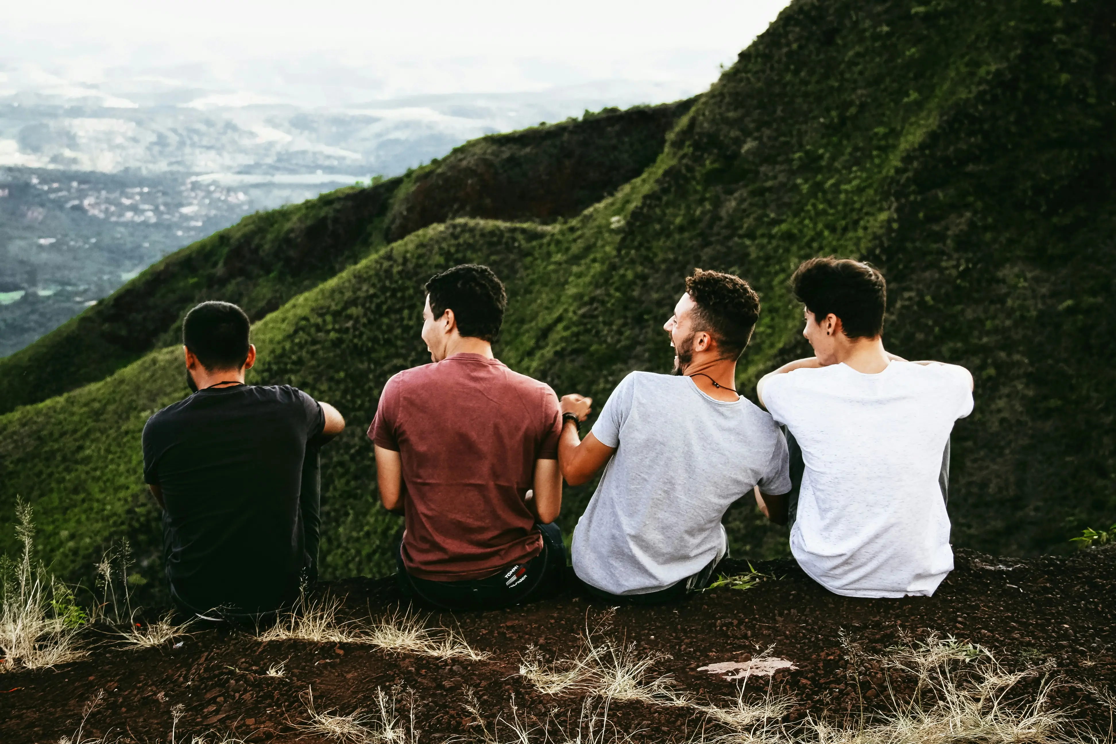 Four uoung people sit on a hill with their backs to the camera overlooking the view of a green landscape