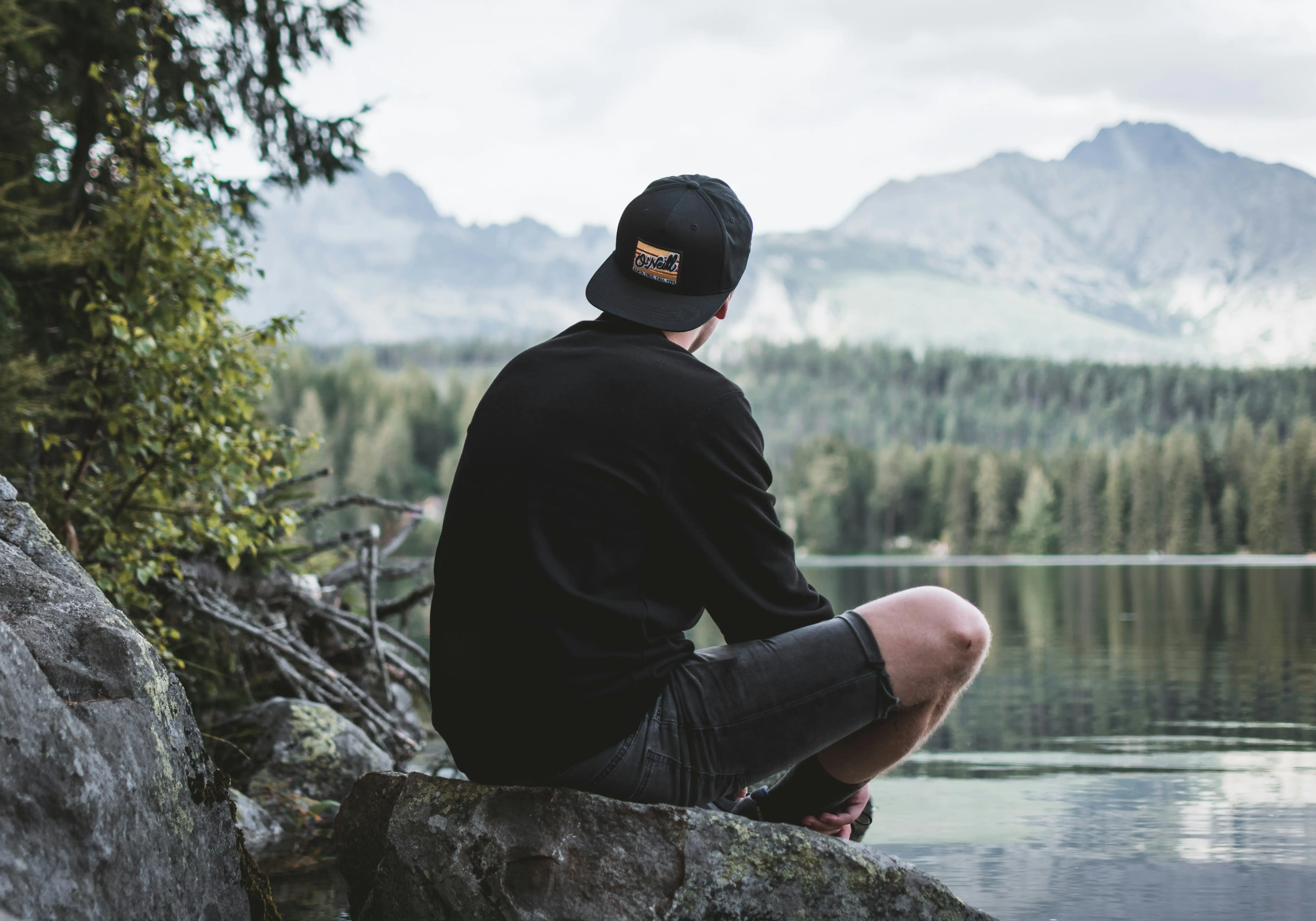 Someone sitting on the edge of a lake looking at the water with his back to the camera