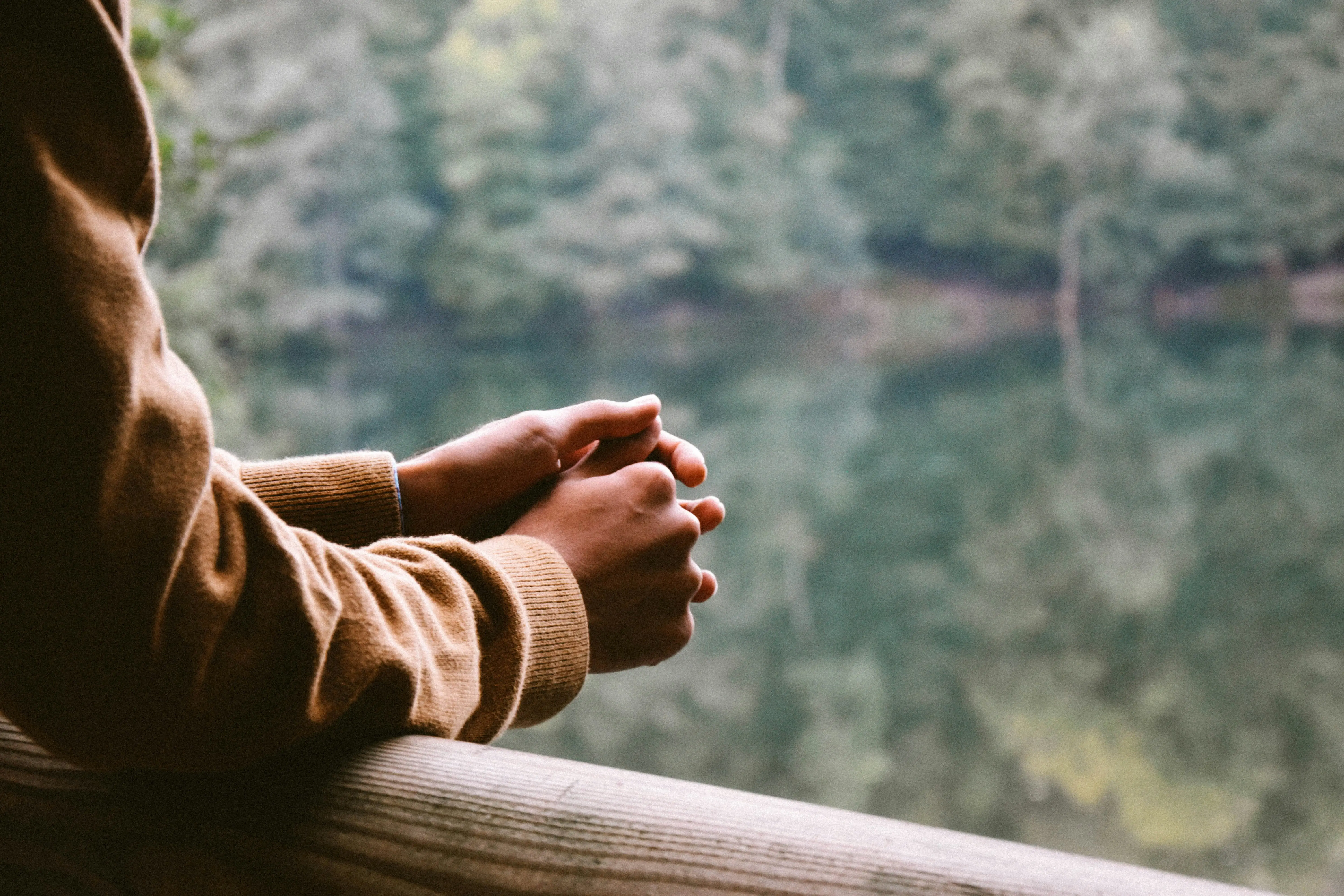 A close up image of someones arms leaning over a wooden fence overlooking a lake